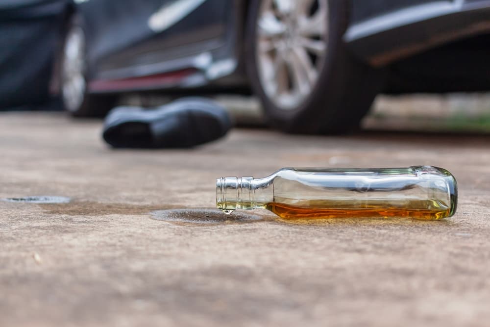 Empty liquor bottle lying on the road near a car, symbolizing a drunk driving car accident.