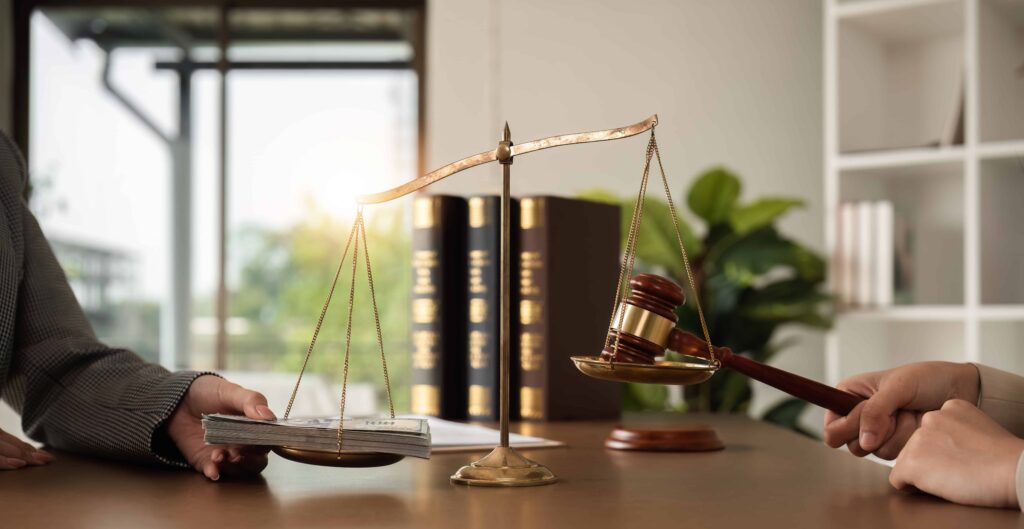 Scales of justice weighing money against a judge&rsquo;s gavel on a desk with law books in the background, symbolizing legal judgment, financial compensation, and justice system